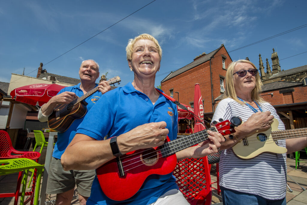 People playing ukeleles outside on a sunny day