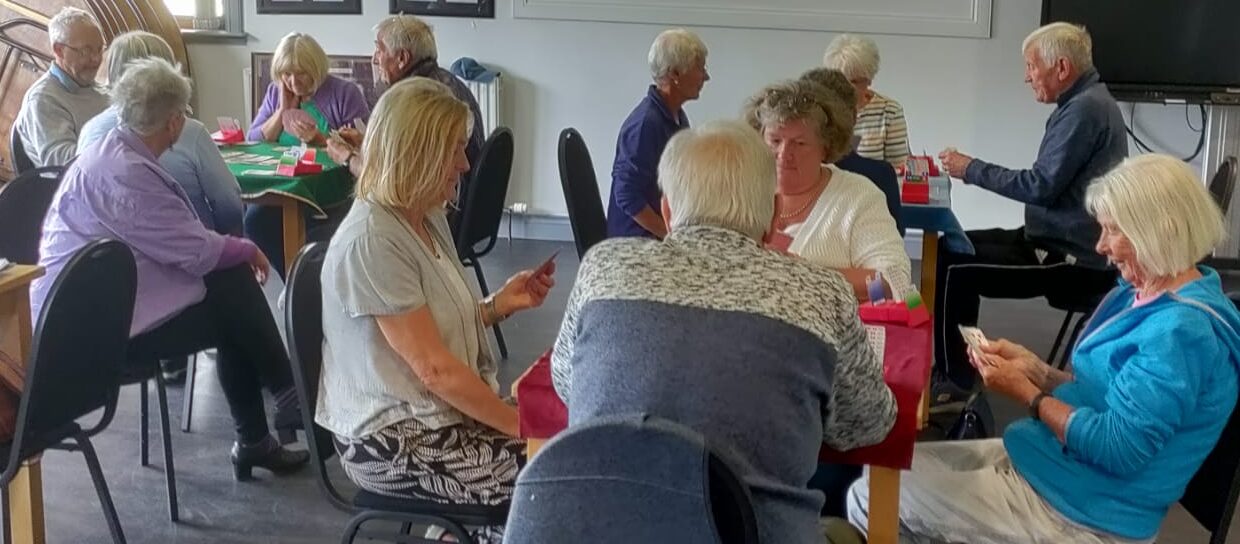 Three groups of four people sitting playing cards and one lady spectating.